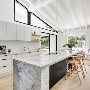 Photo of a mid-sized transitional l-shaped open plan kitchen in Sydney with an undermount sink, flat-panel cabinets, dark wood cabinets, granite benchtops, white splashback, matchstick tile splashback, black appliances, light hardwood floors, with island, beige floor, grey benchtop, exposed beam and vaulted.