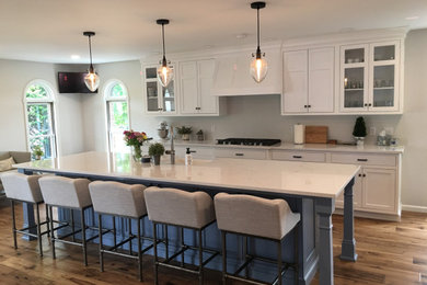Eat-in kitchen - mid-sized contemporary single-wall medium tone wood floor and brown floor eat-in kitchen idea in Other with a farmhouse sink, recessed-panel cabinets, white cabinets, glass countertops, gray backsplash, an island and white countertops