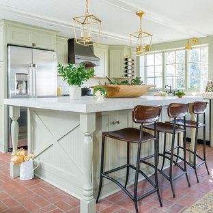 Photo of a mid-sized mediterranean l-shaped eat-in kitchen in Baltimore with a farmhouse sink, quartz benchtops, stainless steel appliances, brick floors, with island, shaker cabinets, green cabinets, white splashback, subway tile splashback and red floor.