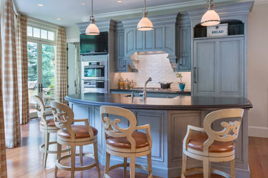 Example of a mid-sized classic single-wall dark wood floor eat-in kitchen design in Boston with a farmhouse sink, raised-panel cabinets, gray cabinets, granite countertops, white backsplash, ceramic backsplash, stainless steel appliances and an island