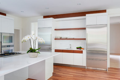 Photo of an expansive contemporary u-shaped kitchen pantry in Boston with flat-panel cabinets, white cabinets, engineered stone countertops, white splashback, ceramic splashback, stainless steel appliances, medium hardwood flooring and an island.