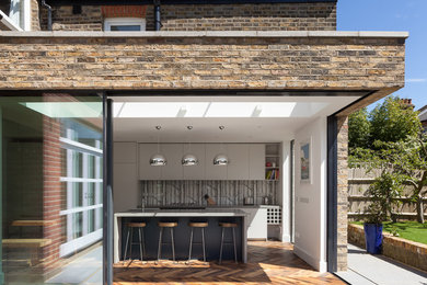 Moderne Wohnküche mit flächenbündigen Schrankfronten, Betonarbeitsplatte, braunem Holzboden, Kücheninsel und braunem Boden in London