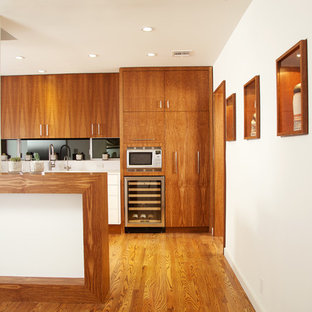 Idées déco pour une cuisine moderne avec un placard à porte plane, un électroménager en acier inoxydable, un plan de travail en bois, une crédence noire, une crédence en feuille de verre et des portes de placard en bois brun.