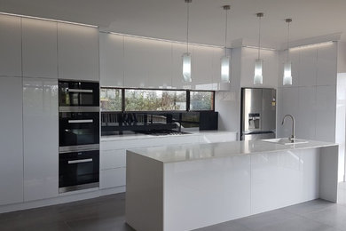 Inspiration for a large contemporary u-shaped kitchen/diner in Perth with a single-bowl sink, glass-front cabinets, white cabinets, engineered stone countertops, black splashback, glass sheet splashback, stainless steel appliances, ceramic flooring, an island, grey floors and white worktops.