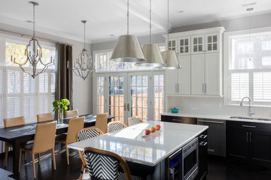 This is an example of a classic l-shaped open plan kitchen in Boston with a submerged sink, shaker cabinets, white cabinets, engineered stone countertops, white splashback, mosaic tiled splashback, stainless steel appliances, dark hardwood flooring, an island and brown floors.