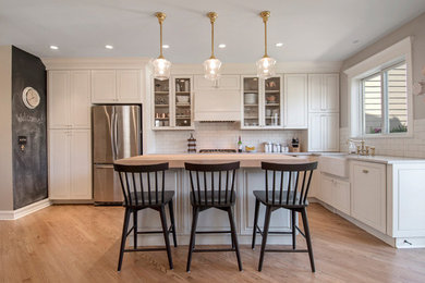 Mid-sized farmhouse l-shaped light wood floor open concept kitchen photo in Chicago with a farmhouse sink, raised-panel cabinets, white cabinets, quartz countertops, white backsplash, subway tile backsplash, stainless steel appliances and an island