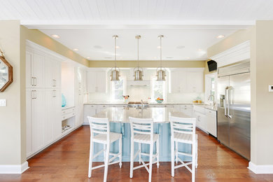 Photo of a nautical kitchen in Other with a belfast sink, shaker cabinets, white cabinets, white splashback, stainless steel appliances, medium hardwood flooring and an island.