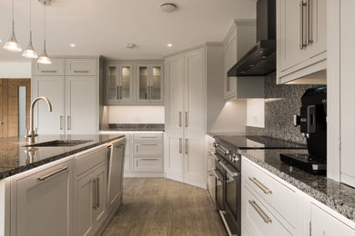 Inspiration for a traditional l-shaped kitchen/diner in Oxfordshire with a built-in sink, shaker cabinets, grey cabinets, granite worktops, grey splashback, granite splashback, black appliances, an island, grey floors and grey worktops.