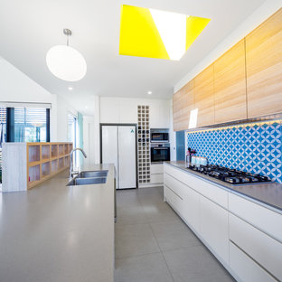 Mid-sized contemporary galley open plan kitchen in Canberra - Queanbeyan with white cabinets, quartz benchtops, blue splashback, cement tile splashback, with island, grey floor, a double-bowl sink, flat-panel cabinets, white appliances and grey benchtop.