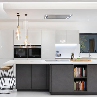 This is an example of a medium sized contemporary galley open plan kitchen in London with flat-panel cabinets, grey cabinets, quartz worktops, grey splashback, stone slab splashback, black appliances, porcelain flooring, an island, grey floors, a submerged sink and white worktops.