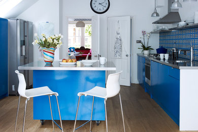 Contemporary galley enclosed kitchen in London with a single-bowl sink, flat-panel cabinets, blue cabinets, multi-coloured splashback, stainless steel appliances, medium hardwood flooring and an island.
