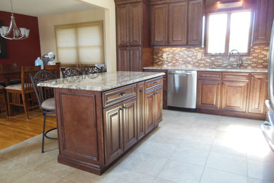 Example of a mid-sized classic porcelain tile and beige floor eat-in kitchen design in New York with raised-panel cabinets, brown cabinets, granite countertops, an island, an undermount sink, brown backsplash, mosaic tile backsplash, stainless steel appliances and beige countertops