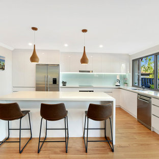 Design ideas for a contemporary l-shaped kitchen in Gold Coast - Tweed with a double-bowl sink, flat-panel cabinets, white cabinets, glass sheet splashback, stainless steel appliances, dark hardwood floors, with island, beige floor and white benchtop.