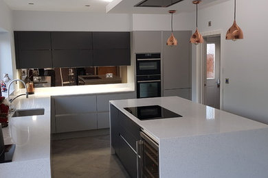 Photo of a medium sized contemporary l-shaped kitchen/diner in Surrey with flat-panel cabinets, grey cabinets, an island, a submerged sink, quartz worktops, white splashback, mirror splashback, stainless steel appliances, vinyl flooring, brown floors and white worktops.