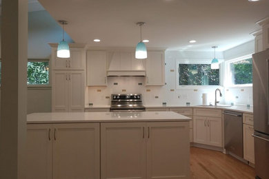 Imagen de cocina comedor minimalista con puertas de armario blancas, electrodomésticos de acero inoxidable, suelo de madera clara y una isla