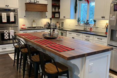 Inspiration for a large transitional l-shaped dark wood floor and brown floor eat-in kitchen remodel in Other with a single-bowl sink, flat-panel cabinets, white cabinets, quartz countertops, white backsplash, subway tile backsplash, stainless steel appliances, an island and black countertops