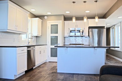 Example of a mid-sized minimalist l-shaped vinyl floor and brown floor eat-in kitchen design in Other with a drop-in sink, shaker cabinets, white cabinets, laminate countertops, white backsplash, ceramic backsplash, stainless steel appliances, an island and gray countertops