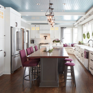 Large traditional separate kitchen in Omaha with a farmhouse sink, shaker cabinets, white cabinets, white splashback, stainless steel appliances, medium hardwood floors and multiple islands.
