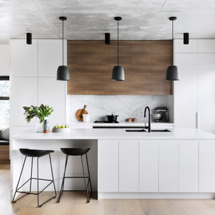 This is an example of a contemporary eat-in kitchen in Melbourne with a double-bowl sink, flat-panel cabinets, white cabinets, grey splashback, panelled appliances, light hardwood floors, with island, beige floor and white benchtop.