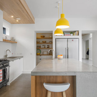 Cette image montre une cuisine ouverte design de taille moyenne avec un évier posé, un placard à porte plane, des portes de placard blanches, un plan de travail en béton, une crédence blanche, un électroménager en acier inoxydable, béton au sol, un îlot central, un sol gris, un plan de travail gris et un plafond en lambris de bois.