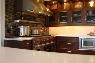 Eclectic u-shaped eat-in kitchen photo in Philadelphia with recessed-panel cabinets, medium tone wood cabinets, solid surface countertops, metallic backsplash, mosaic tile backsplash and stainless steel appliances
