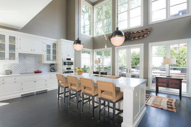 Example of a huge trendy single-wall dark wood floor and brown floor open concept kitchen design in Other with a single-bowl sink, raised-panel cabinets, white cabinets, marble countertops, white backsplash, ceramic backsplash, stainless steel appliances and an island