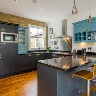Photo of a medium sized traditional u-shaped kitchen in London with a double-bowl sink, metallic splashback, stainless steel appliances, medium hardwood flooring, a breakfast bar, brown floors, black worktops, shaker cabinets and blue cabinets.