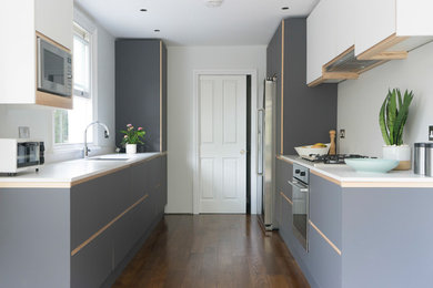 Inspiration for a medium sized modern galley kitchen in London with an integrated sink, engineered stone countertops, white splashback, stone tiled splashback, stainless steel appliances, medium hardwood flooring and white worktops.