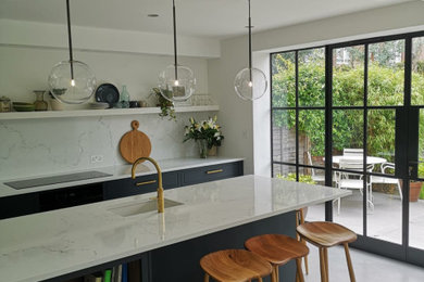 Photo of a medium sized contemporary galley kitchen/diner in London with a built-in sink, shaker cabinets, blue cabinets, marble worktops, white splashback, marble splashback, integrated appliances, concrete flooring, an island, grey floors and white worktops.