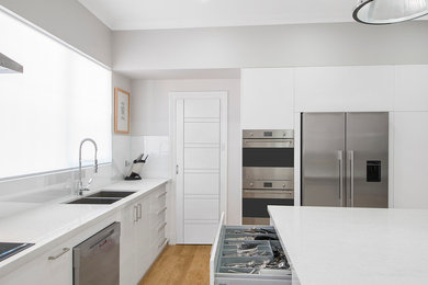 Foto di una grande cucina design con lavello a doppia vasca, top in quarzo composito, paraspruzzi bianco, paraspruzzi con lastra di vetro e elettrodomestici in acciaio inossidabile