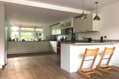 Design ideas for a large traditional u-shaped open plan kitchen in Surrey with a submerged sink, shaker cabinets, grey cabinets, quartz worktops, grey splashback, ceramic splashback, stainless steel appliances, laminate floors, a breakfast bar, brown floors and brown worktops.