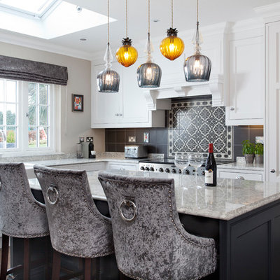 Trendy l-shaped dark wood floor and brown floor kitchen photo in Dublin with a farmhouse sink, shaker cabinets, white cabinets, gray backsplash, mosaic tile backsplash, an island and gray countertops
