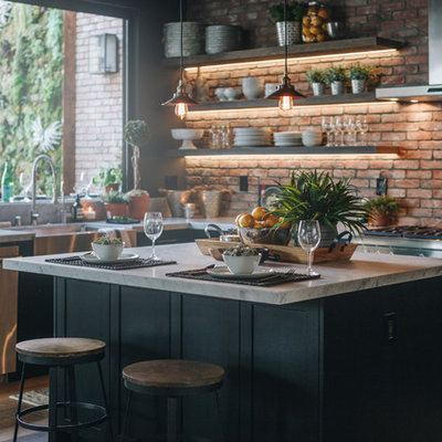 Large urban l-shaped laminate floor and brown floor eat-in kitchen photo in Los Angeles with a farmhouse sink, shaker cabinets, black cabinets, red backsplash, brick backsplash, stainless steel appliances, an island and white countertops