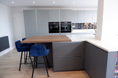 Design ideas for a large modern single-wall kitchen/diner in Other with an integrated sink, flat-panel cabinets, grey cabinets, quartz worktops, black splashback, metro tiled splashback, black appliances, laminate floors, an island, brown floors and white worktops.