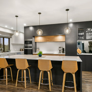 Foto di una cucina minimal con lavello da incasso, ante lisce, ante nere, paraspruzzi bianco, paraspruzzi a specchio, pavimento in legno massello medio, isola, pavimento marrone e top giallo