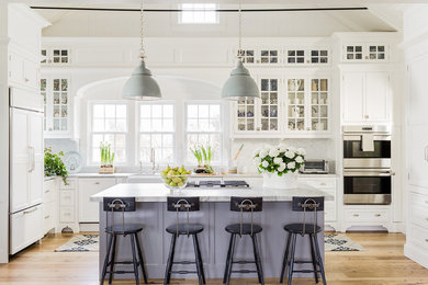 Example of a large classic light wood floor kitchen design in Boston with a farmhouse sink, white cabinets, quartzite countertops, white backsplash, paneled appliances, an island and glass-front cabinets
