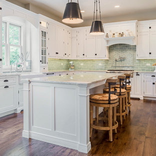 Mid-sized transitional l-shaped medium tone wood floor eat-in kitchen photo in Chicago with a farmhouse sink, shaker cabinets, white cabinets, quartzite countertops, green backsplash, ceramic backsplash, paneled appliances and an island