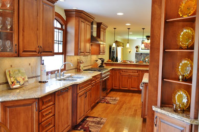 Inspiration for a huge timeless l-shaped medium tone wood floor eat-in kitchen remodel in New York with a double-bowl sink, raised-panel cabinets, medium tone wood cabinets, granite countertops, beige backsplash, ceramic backsplash, stainless steel appliances and an island