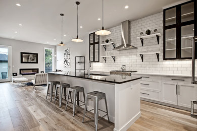 Inspiration for a transitional galley light wood floor kitchen remodel in Calgary with an undermount sink, shaker cabinets, white cabinets, quartz countertops, white backsplash, ceramic backsplash, stainless steel appliances and an island