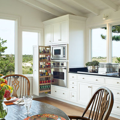 Example of a classic medium tone wood floor eat-in kitchen design in New York with stainless steel appliances, shaker cabinets, white cabinets and an island