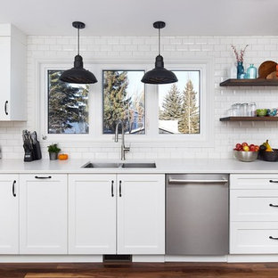 Inspiration for a mid-sized transitional l-shaped medium tone wood floor eat-in kitchen remodel in Orange County with a double-bowl sink, shaker cabinets, white cabinets, solid surface countertops, white backsplash, subway tile backsplash, stainless steel appliances and no island