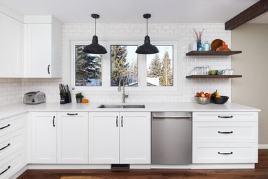 Inspiration for a mid-sized transitional l-shaped medium tone wood floor eat-in kitchen remodel in Orange County with a double-bowl sink, shaker cabinets, white cabinets, solid surface countertops, white backsplash, subway tile backsplash, stainless steel appliances and no island