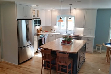 Mid-sized cottage chic l-shaped light wood floor eat-in kitchen photo in Charlotte with a drop-in sink, recessed-panel cabinets, quartz countertops, white backsplash, subway tile backsplash, stainless steel appliances and an island
