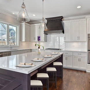 Cette image montre une grand cuisine traditionnelle en L fermée avec un évier encastré, un placard à porte shaker, des portes de placard blanches, une crédence blanche, une crédence en carrelage métro, un électroménager en acier inoxydable, un sol en bois brun, un îlot central et un plan de travail en granite.