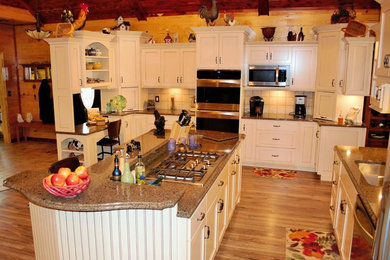 Photo of a large country l-shaped kitchen/diner in St Louis with a double-bowl sink, white cabinets, beige splashback, stainless steel appliances, light hardwood flooring and an island.