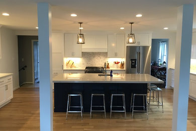 Example of a mid-sized transitional u-shaped brown floor open concept kitchen design in DC Metro with an undermount sink, shaker cabinets, white cabinets, gray backsplash, stainless steel appliances, an island and white countertops