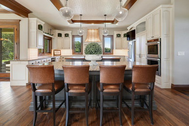 Example of a classic u-shaped dark wood floor and brown floor kitchen design in Other with raised-panel cabinets, white cabinets, beige backsplash, stainless steel appliances and two islands