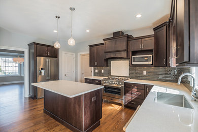 Example of a large transitional l-shaped light wood floor and brown floor kitchen design in New York with an undermount sink, shaker cabinets, dark wood cabinets, quartzite countertops, black backsplash, glass tile backsplash, stainless steel appliances and an island