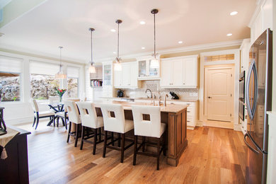 Example of a large transitional l-shaped light wood floor eat-in kitchen design in Vancouver with an undermount sink, recessed-panel cabinets, white cabinets, granite countertops, beige backsplash, stone tile backsplash, stainless steel appliances and an island