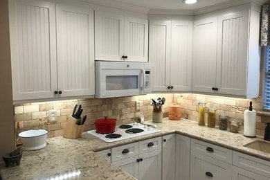 Example of a small classic u-shaped enclosed kitchen design in Houston with an undermount sink, louvered cabinets, white cabinets, laminate countertops, beige backsplash, stone tile backsplash, white appliances and a peninsula